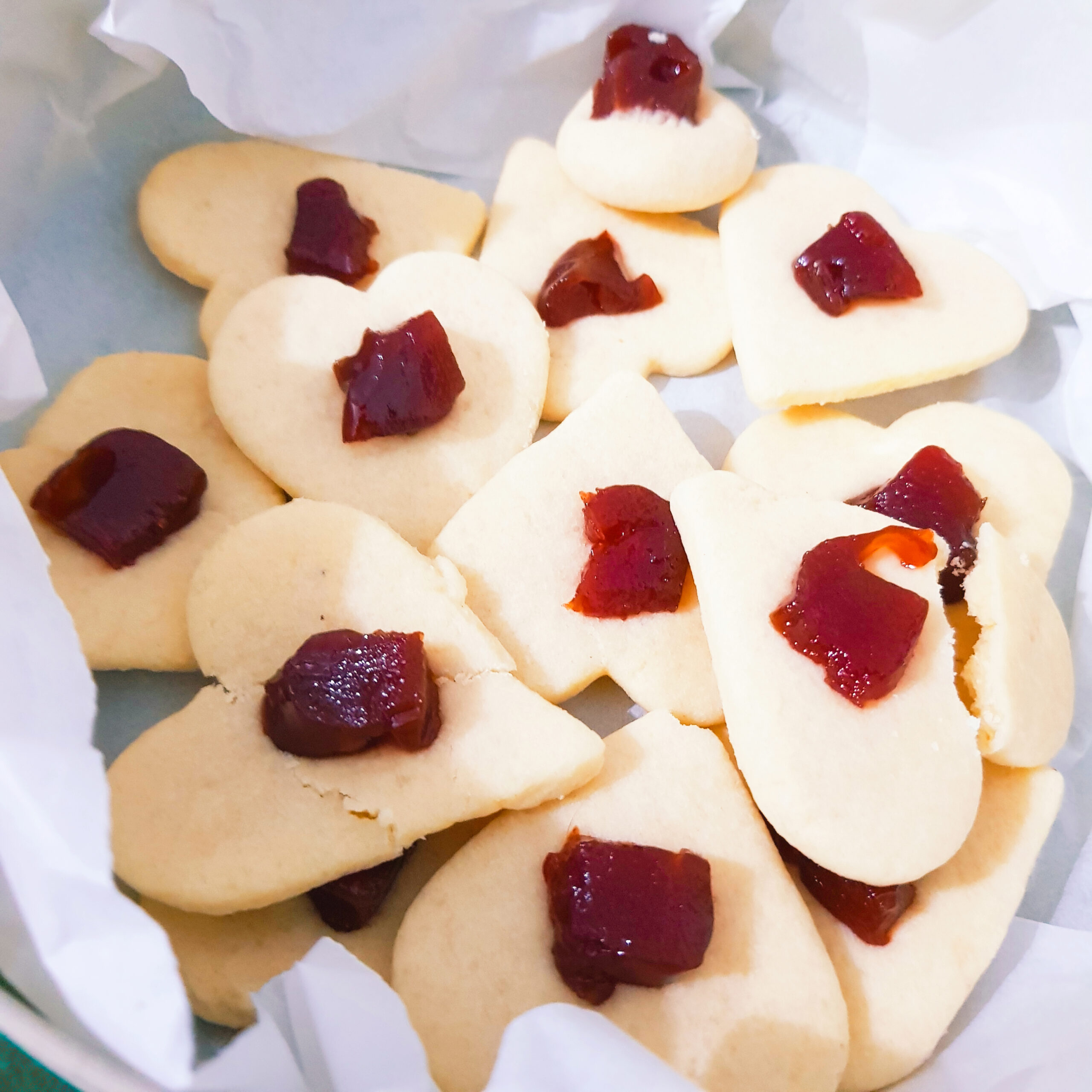biscoitos cor creme em formato de coração, com uma bolinha vermelha de goiabada no centro